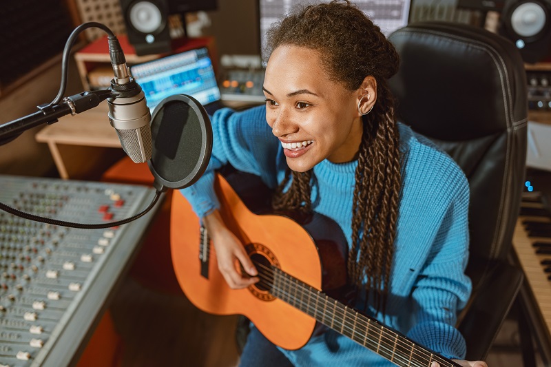 Passionate stunning attractive African American woman singer guitarist plays the guitar and records new cool song in professional sound recording studio Christian Gospel Music